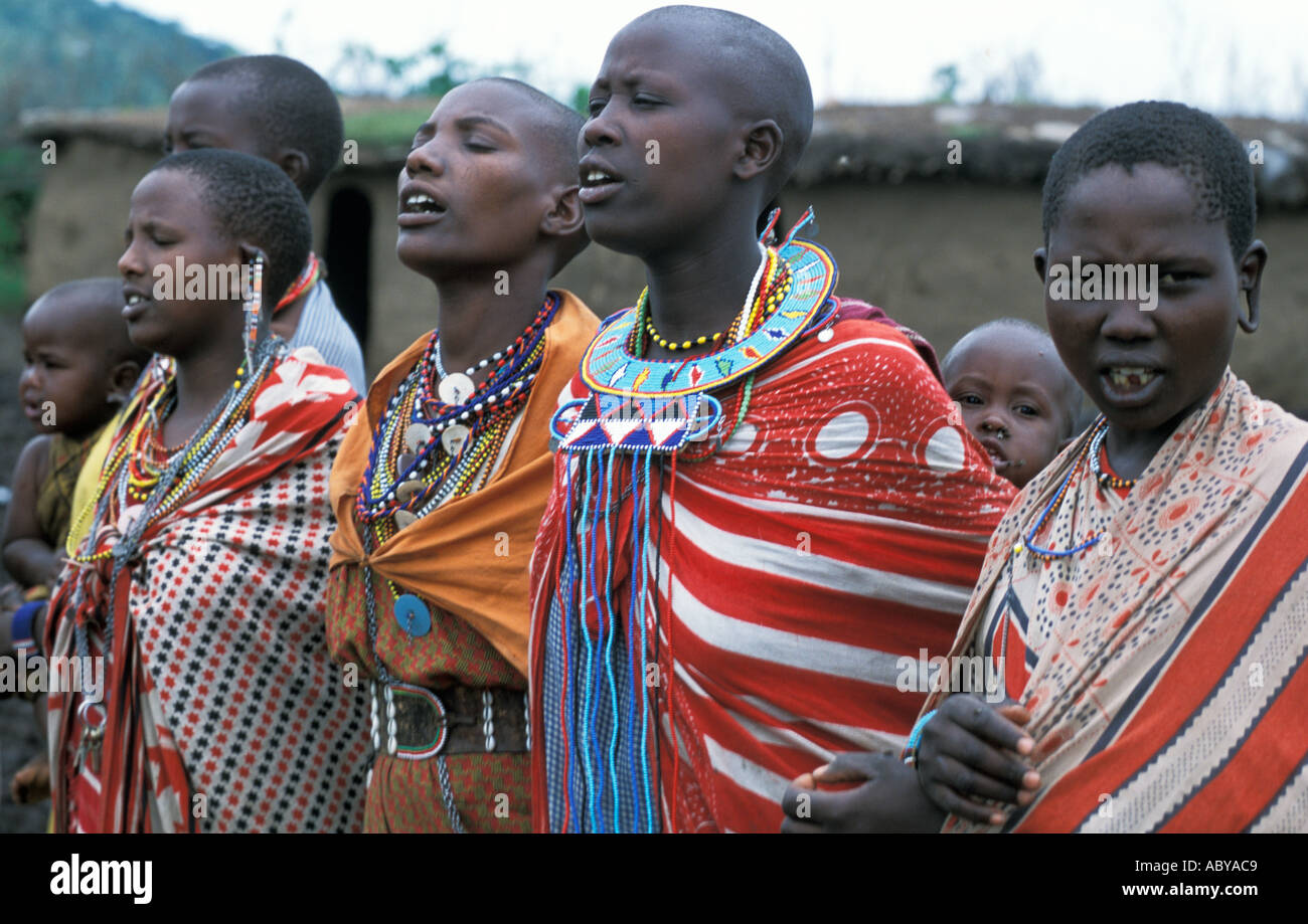 KENYA Masai Mara National Reserve Masai women in traditional kanga cloths and beaded jewelry sing in their manyatta Stock Photo