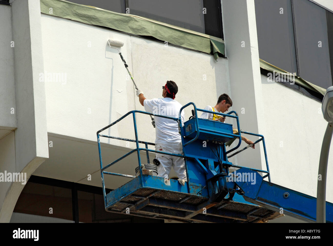 Painters on a rented portable elevator lift paint the exterior of