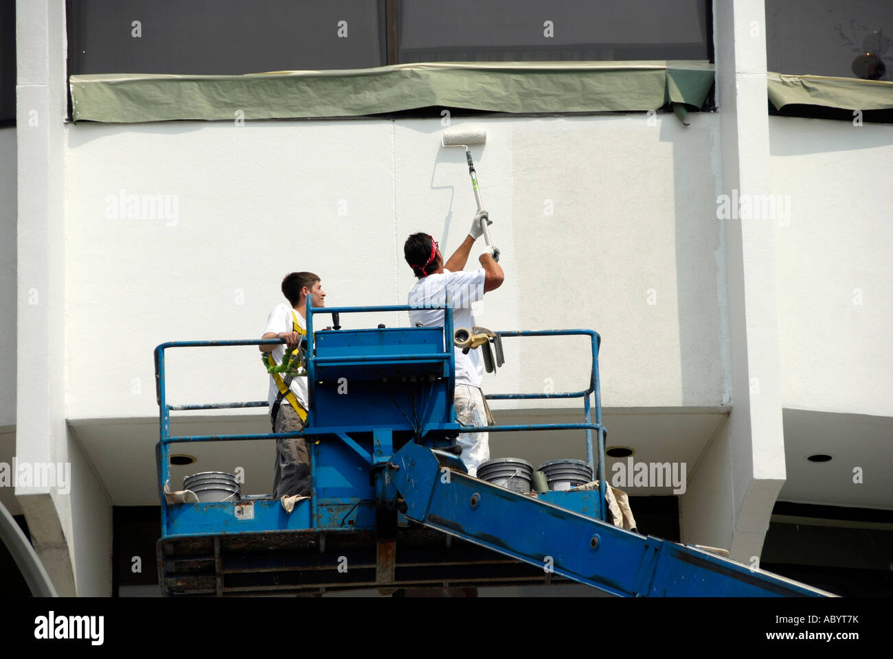 Painters on a rented portable elevator lift paint the exterior of