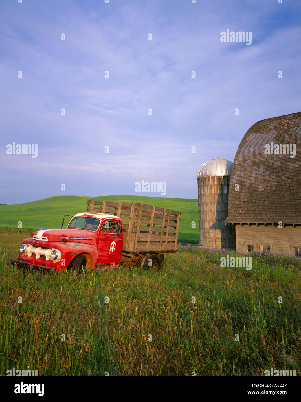 Whitman County WA: Vintage red Ford flatbed truck parked in front of a weathered barn and silo in summer Stock Photo