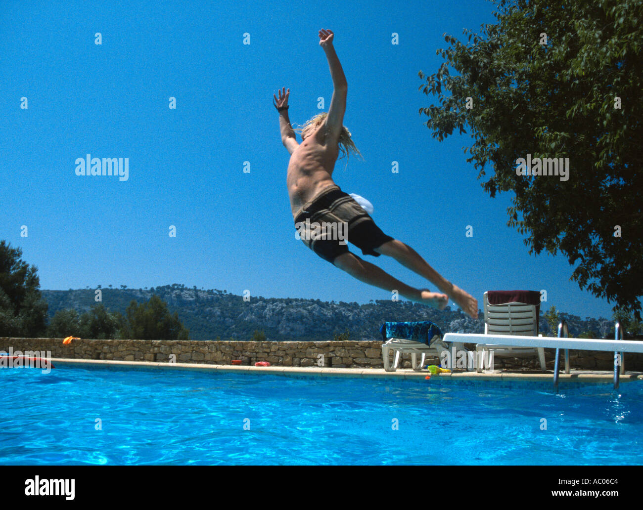 Teenage boy somersaulting off diving board into swimming pool villa