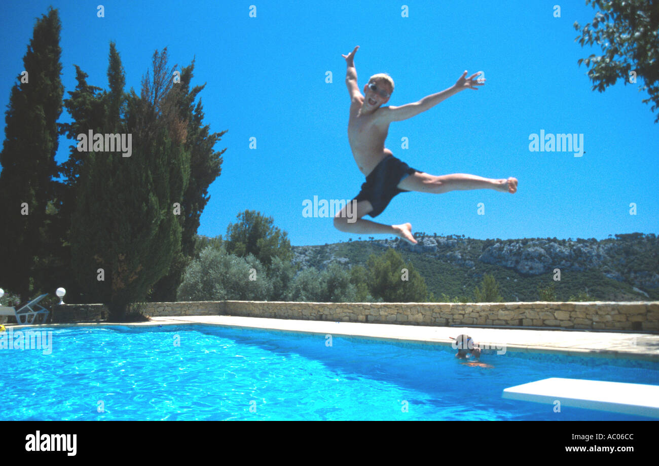 Teenage boy jumps for joy off diving board into villa swimming pool