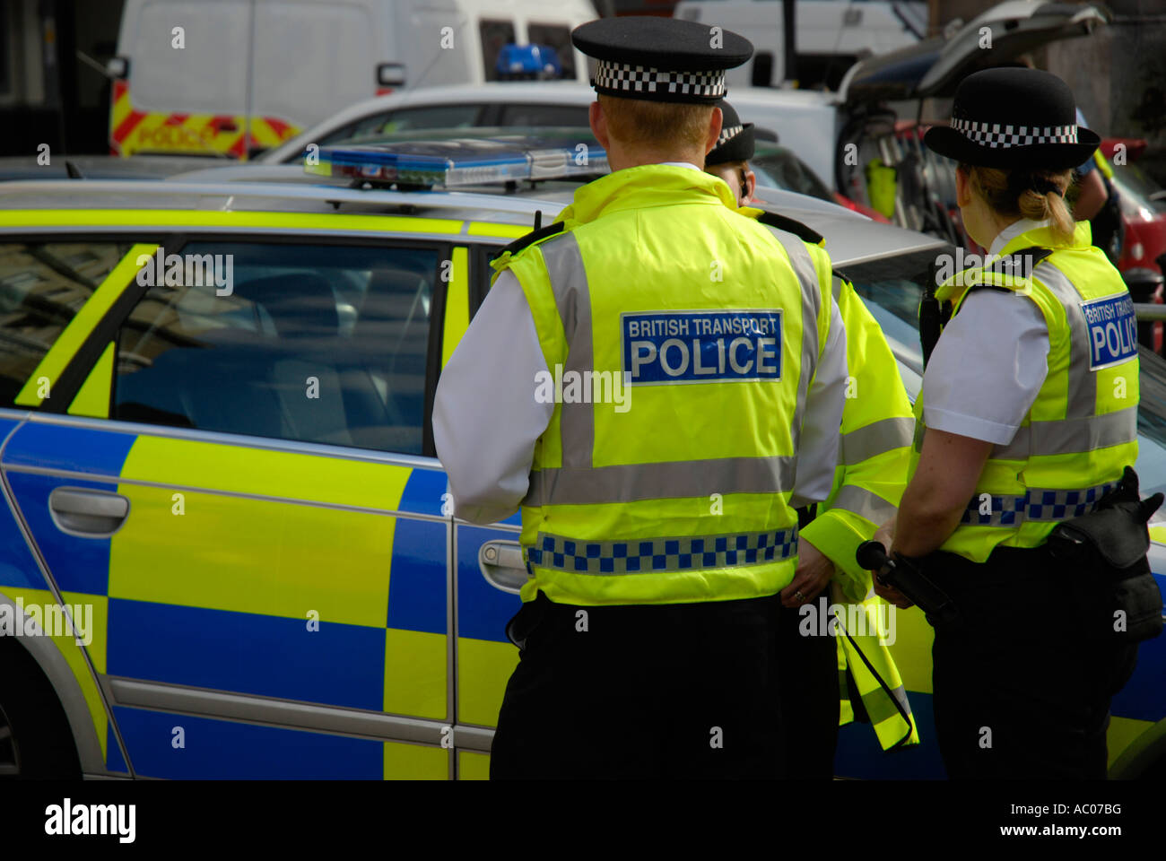 British transport police officers in yellow jackets standing next to yellow and blue coloured police car Stock Photo