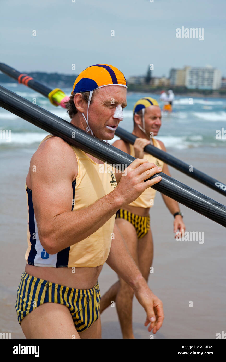Surf lifesavers in club colours carry oars on their shoulders on Cronulla Beach The lifesavers are competing in surfboat races Stock Photo