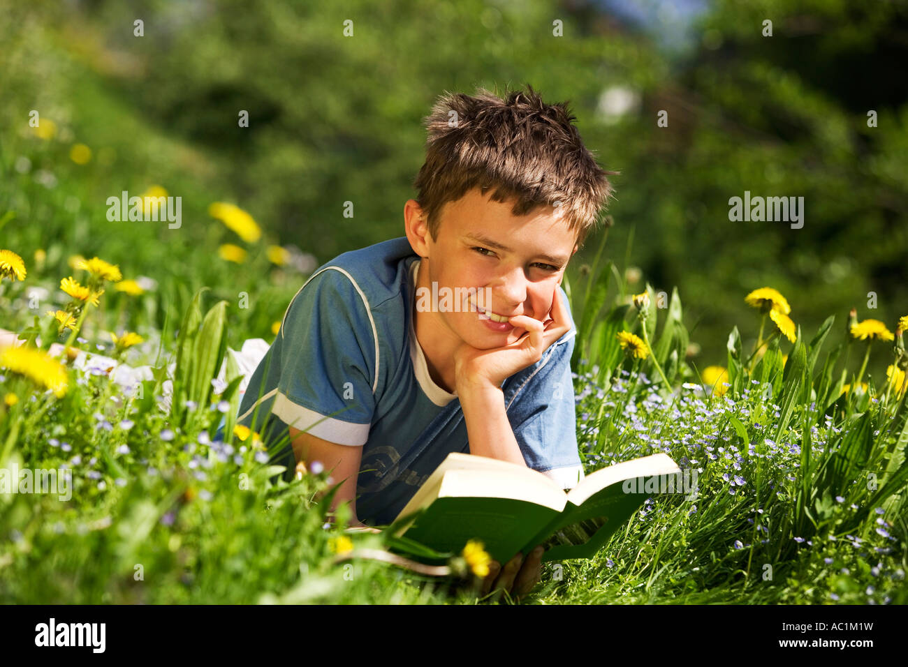 Boy in field reading book, resting head on hand Stock Photo