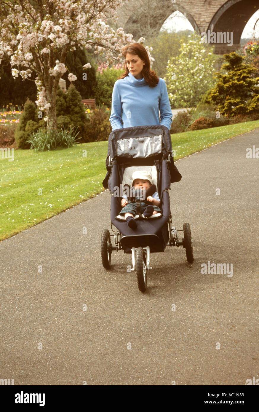 Mother pushing her baby son in a pram in a park looking depressed and unhappy Stock Photo