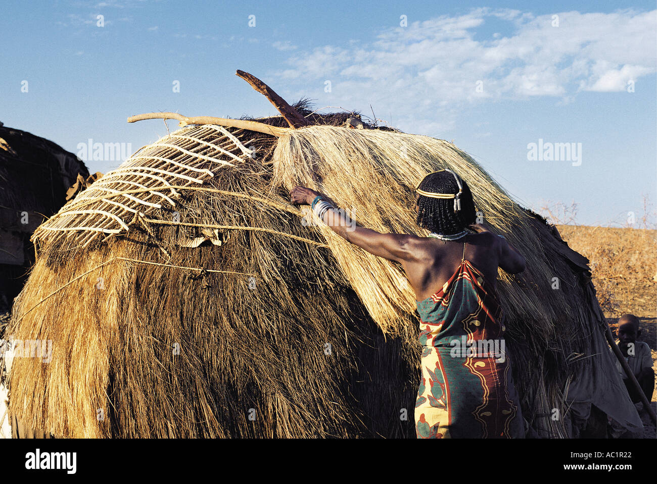 Gabbra married woman placing a sisal mat that she has just finished weaving on the roof of her hut Stock Photo