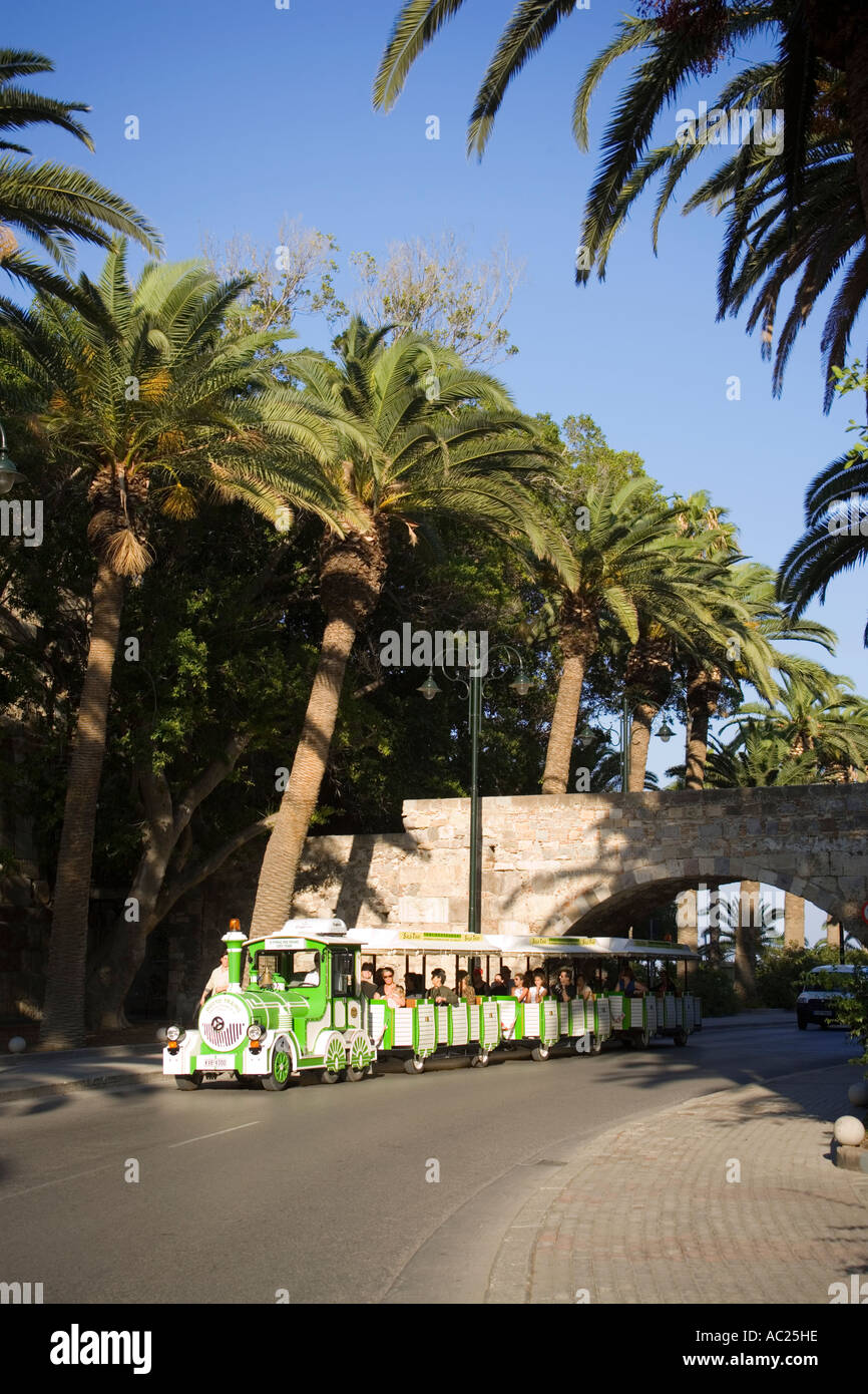 A sightseeing tour train passing a stone bridge at an avenue with plams Kos Town Kos Greece Stock Photo
