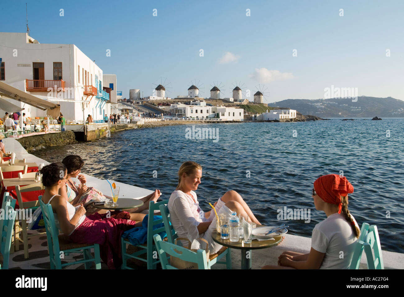 People sitting in restaurants and bars directly at sea windmills in background Little Venice Mykonos Town Mykonos Greece Stock Photo