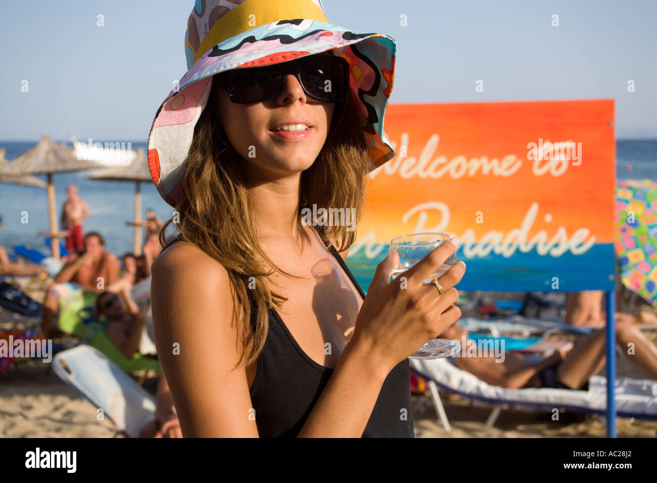 Woman with sunglasses and crazy hat holding a glass of water knowing as a centrum of gays and nudism Psarou Mykonos Greece Stock Photo