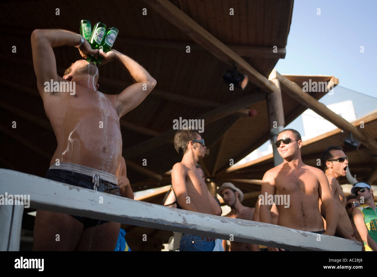 Man drinking four bottles of beer all at once during a beach party of the Super Paradise Club at Super Paradise Beach of gays an Stock Photo