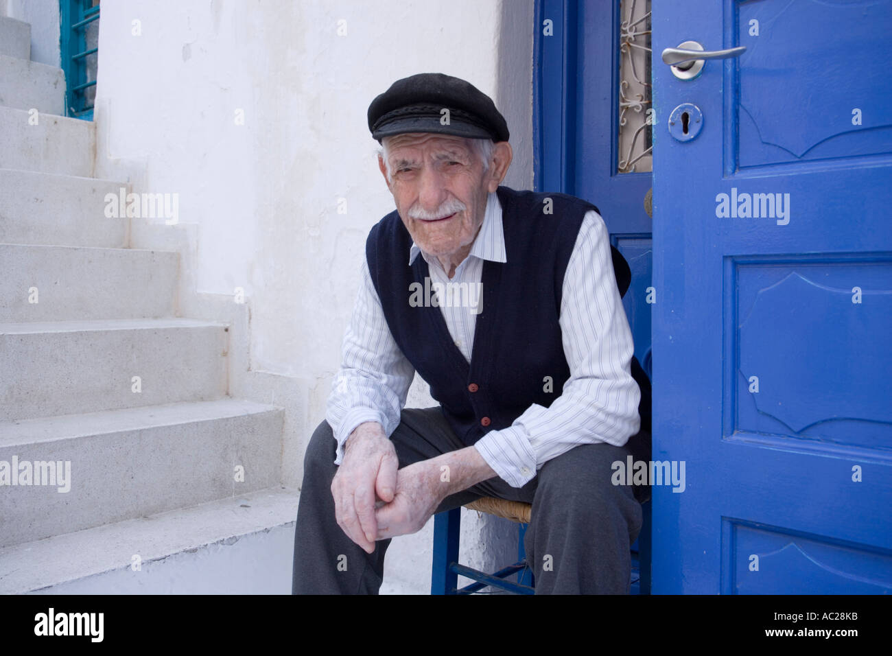 A local old man sitting in front of a white house Mykonos Town Mykonos Greece Stock Photo