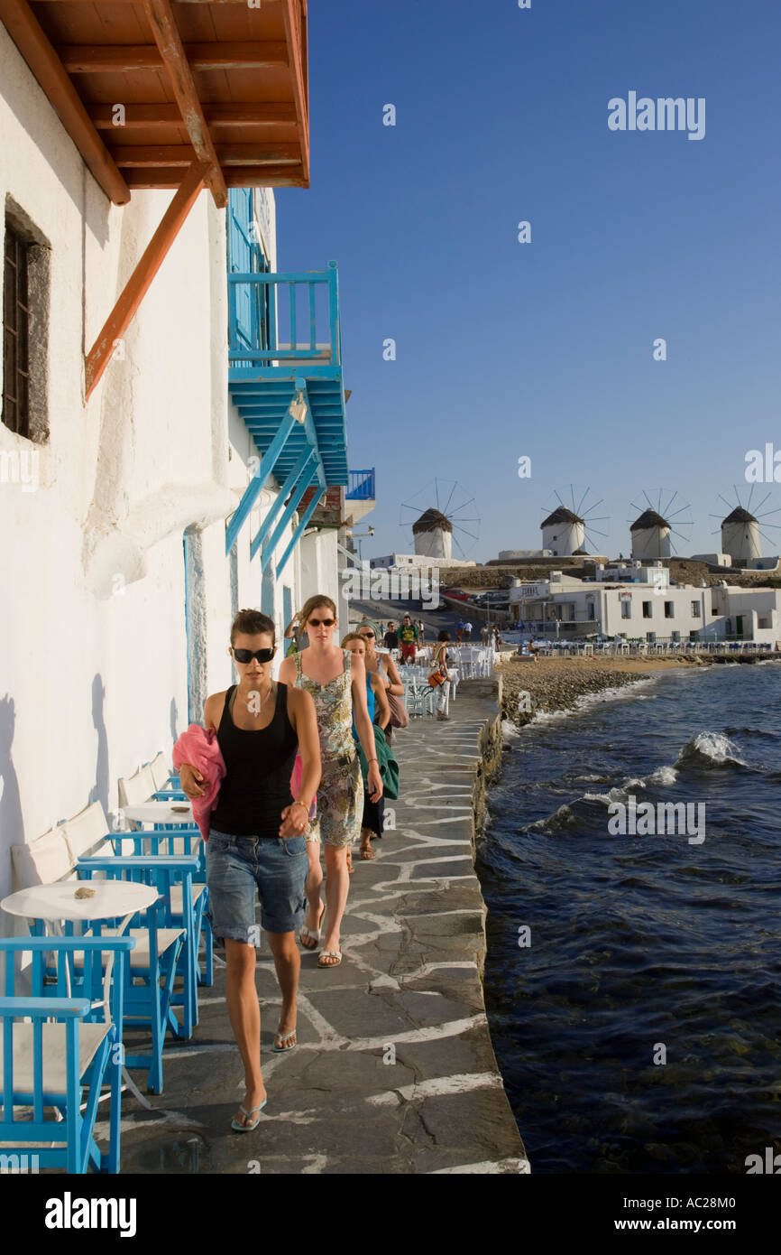 Women strolling along restaurants and bars at bank windmills in background Little Venice Mykonos Town Mykonos Greece Stock Photo