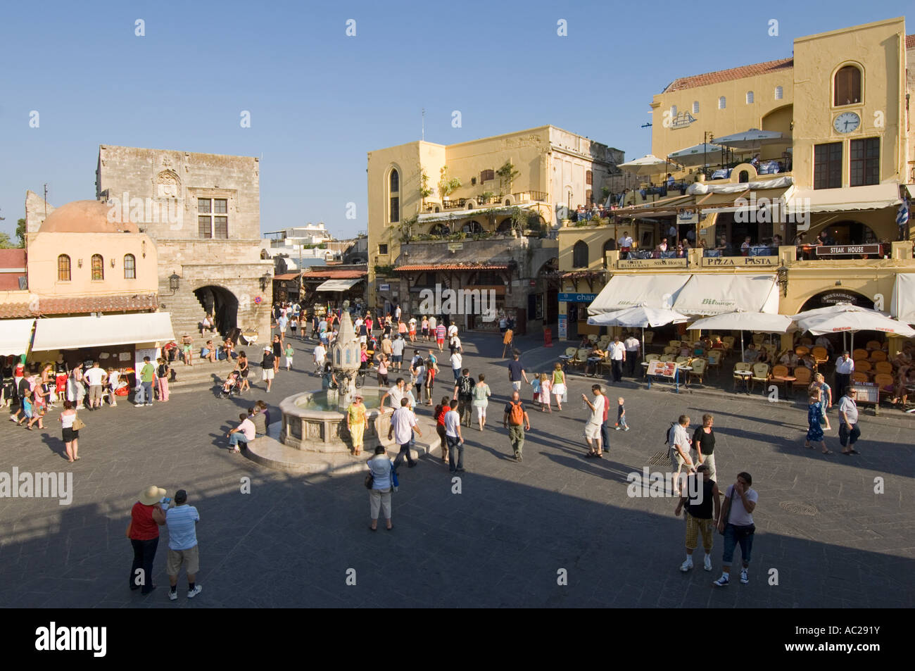 A wide angle view of tourists around the fountain in Ippokratous Square in the centre of Rhodes Old Town. Stock Photo