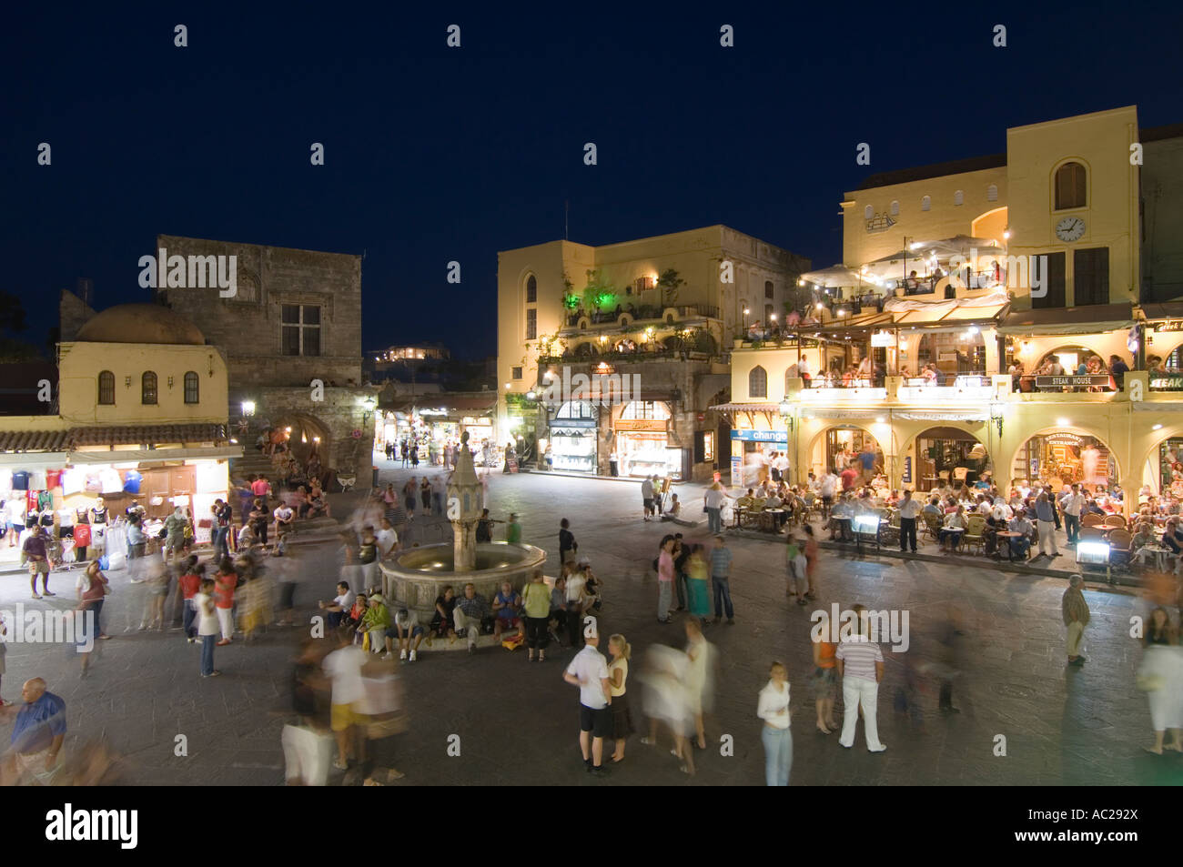 A wide angle evening night view of tourists around the fountain in Ippokratous Square in the centre of Rhodes Old Town. Stock Photo