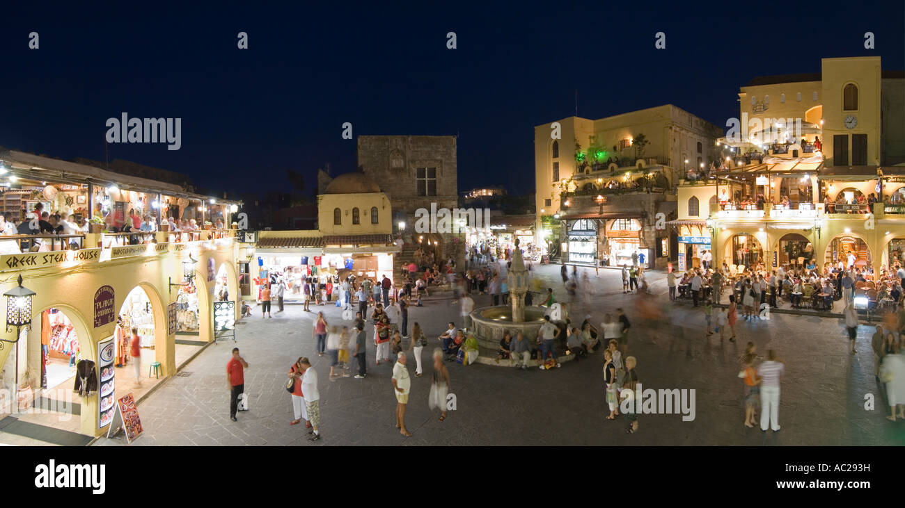 A two picture stitch panoramic evening night view of tourists around the fountain in Ippokratous Square in Rhodes Old Town. Stock Photo