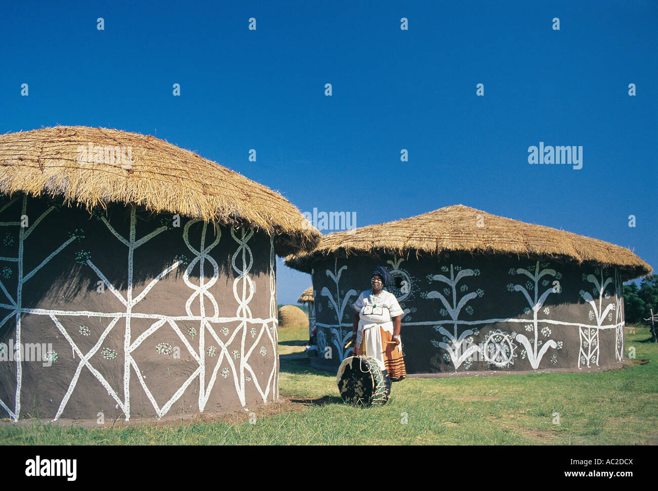 A woman with a drum outside traditional Xhosa village of painted houses