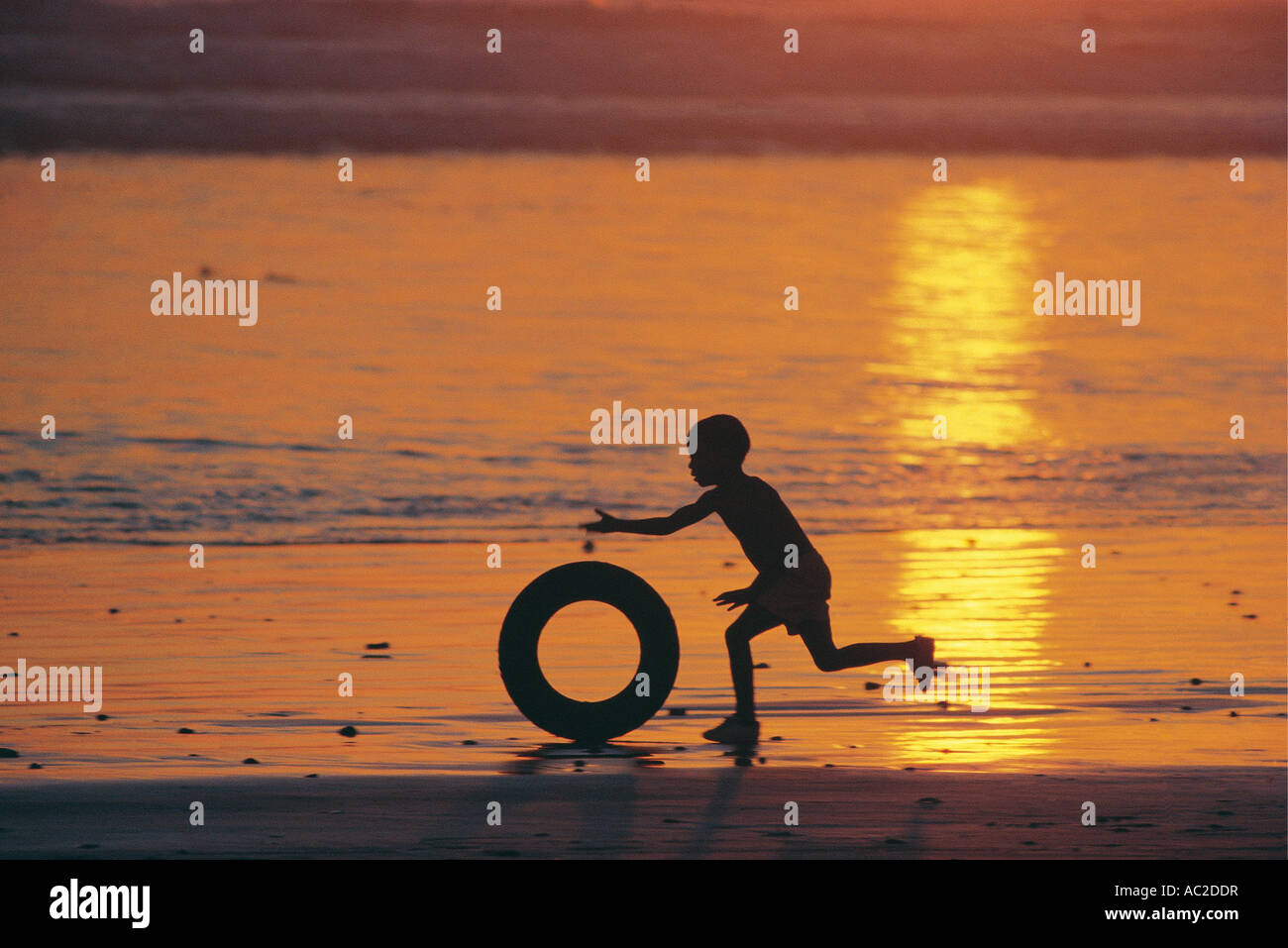 Child playing by rolling a tyre along the beach at sunset Bloubergstrand Cape Town South Africa Stock Photo