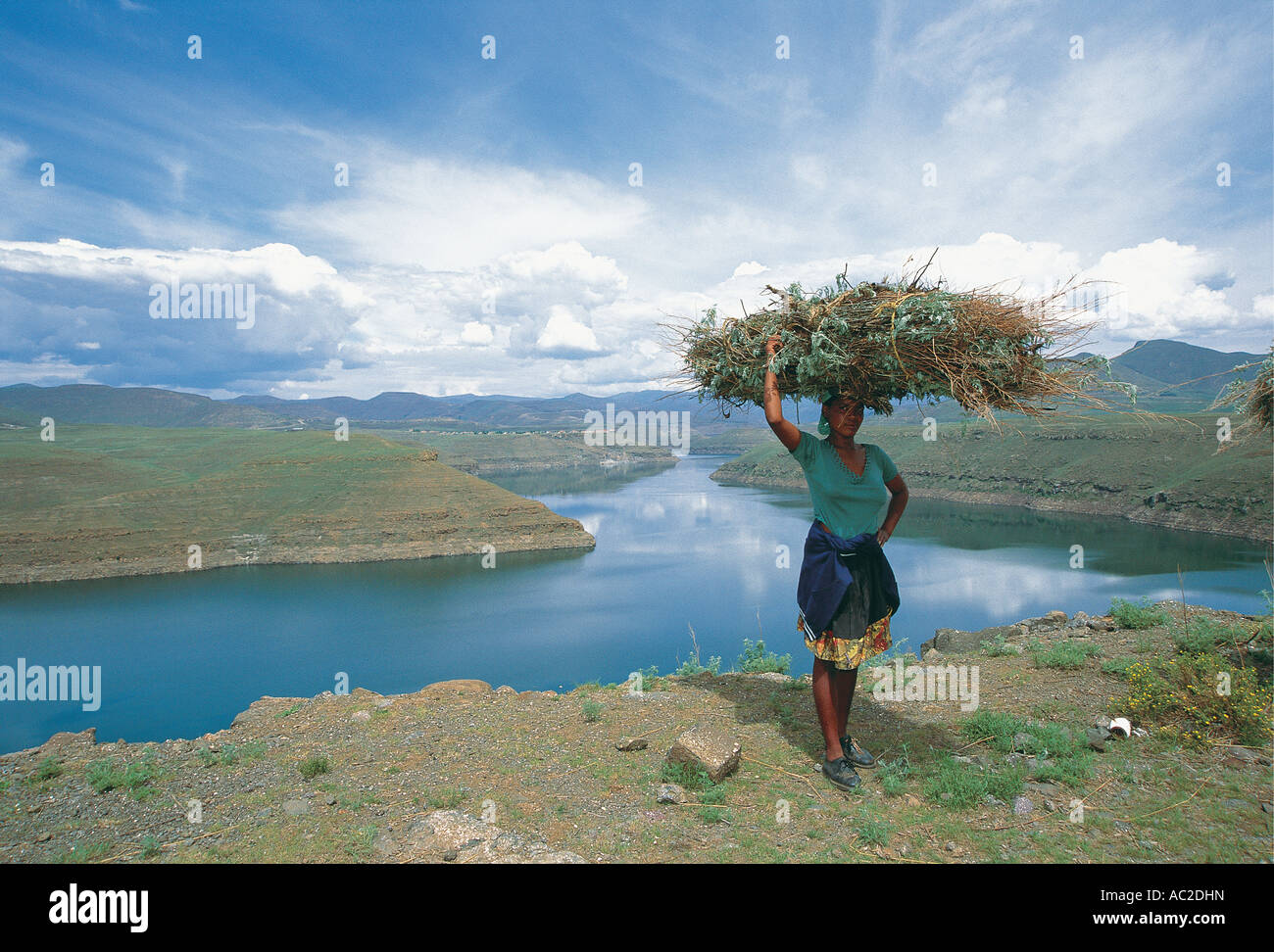 Woman carrying heavy loads on heads Katse Dam behind provides water for South Africa and Lesotho Stock Photo
