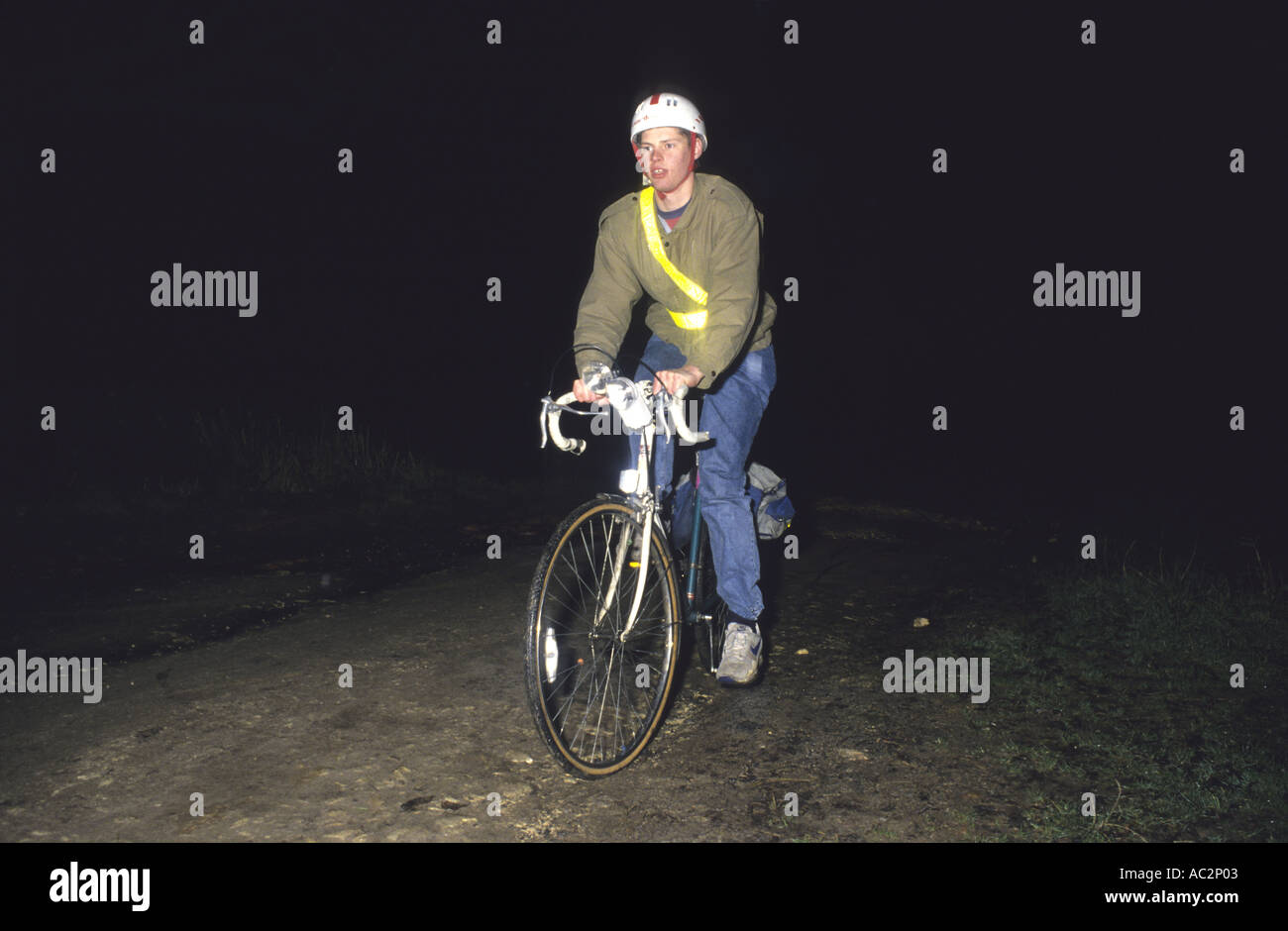 cyclist cycling down country road at night wearing safety reflective clothing illuminated by
