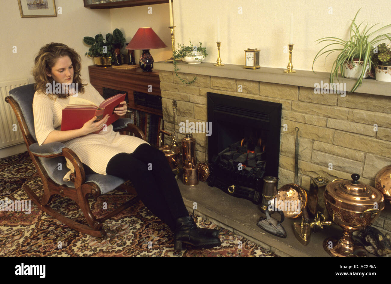 lady relaxing by the fireside reading a book in home Stock Photo
