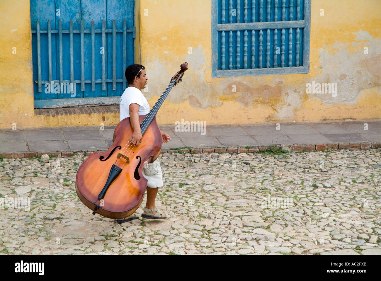 Cuba - Man musician walking down Simon Bolivar carrying a double bass in Trinidad, Cuba Stock Photo