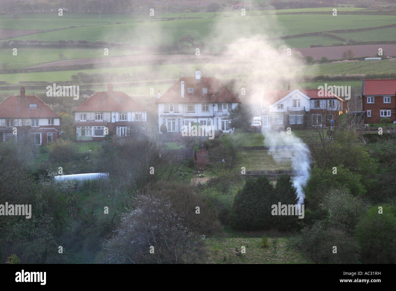 Smoke rising from garden fires on housing estate on a calm wind free evening. Stock Photo