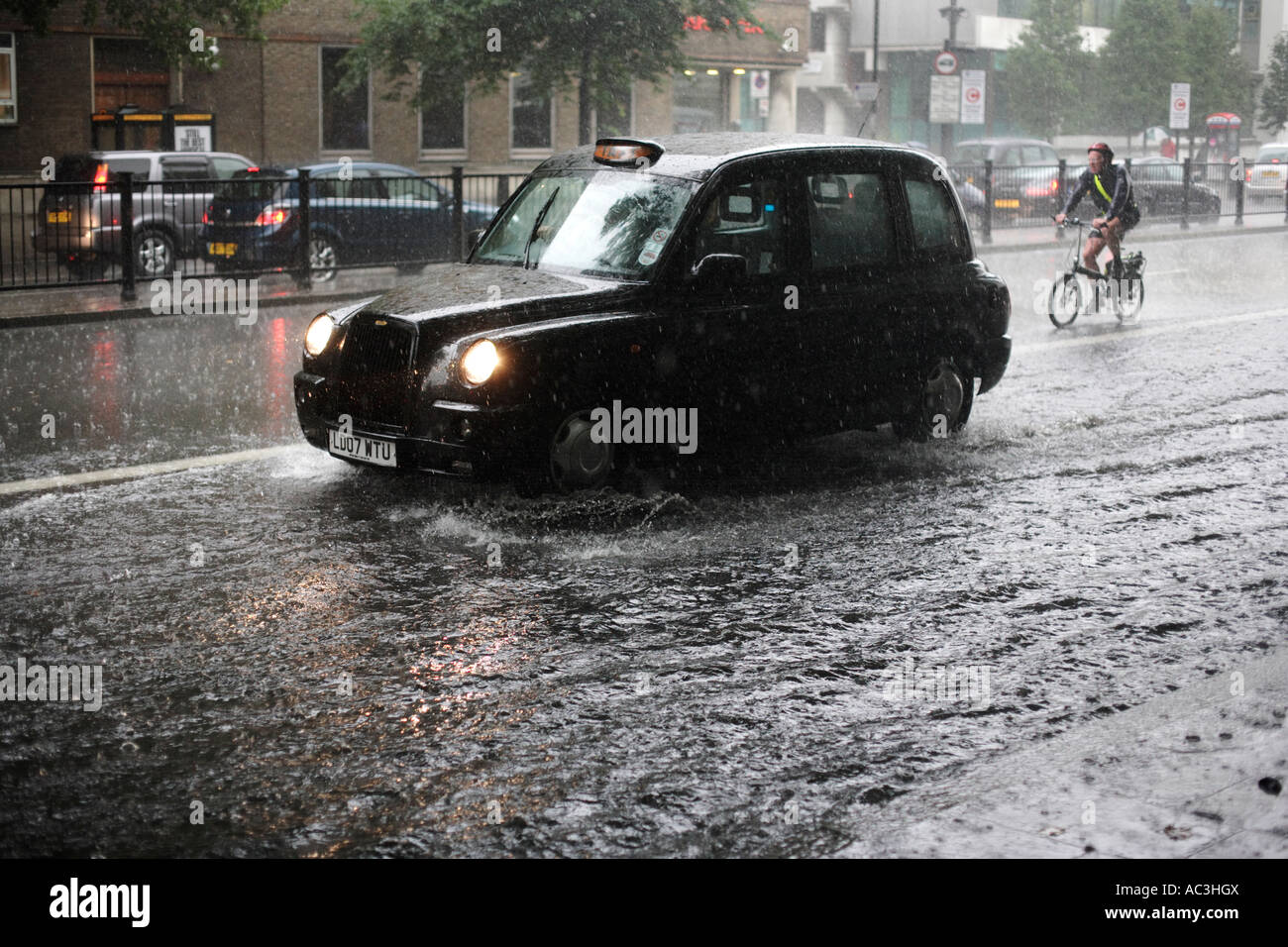 A taxi cab and cyclist make their way along a flooded Marylebone Road in London, during a summer rain storm Stock Photo