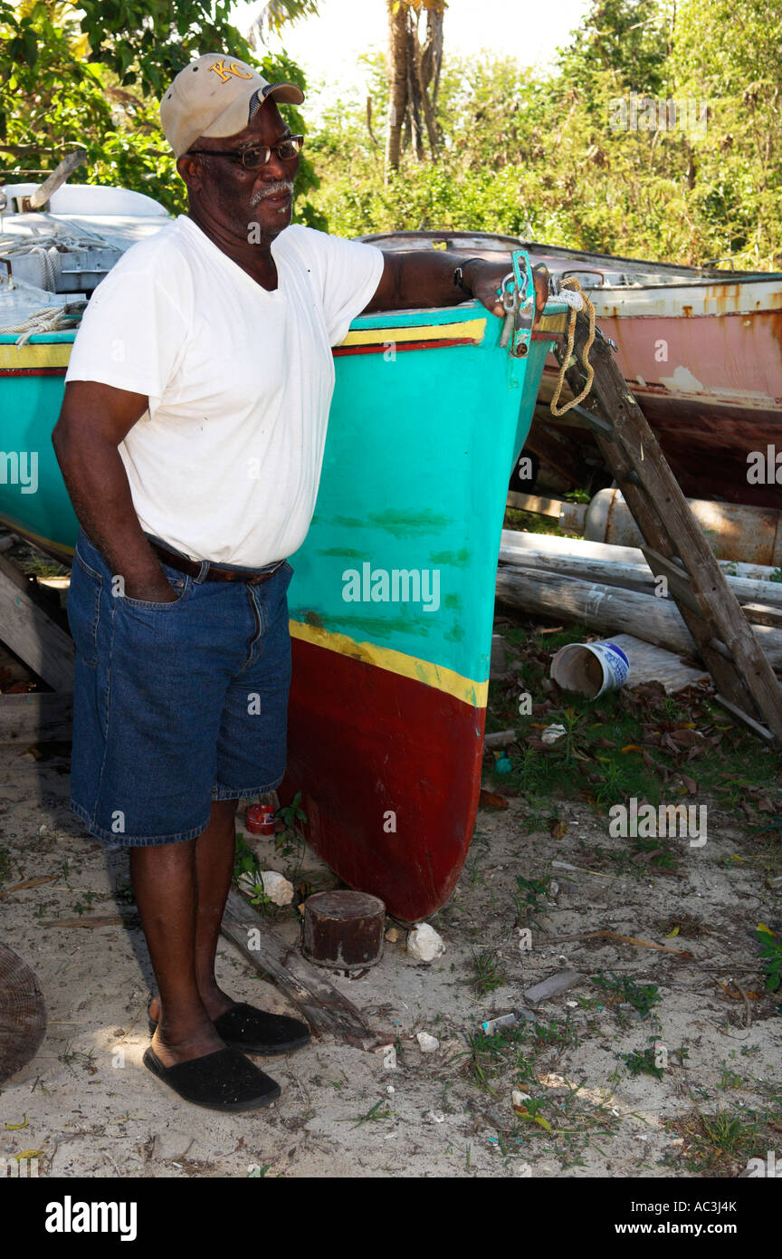 Old retired Black Bahamian boat builder with some of his old boats Andros Island Bahamas Stock Photo