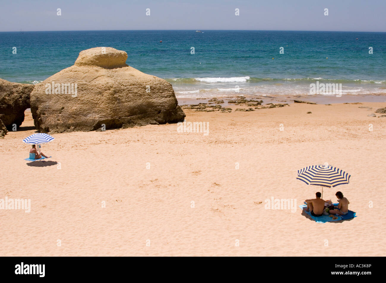 Family on beach sheltering under parasols on an almost deserted beach of Vale do Garrao in the Algarve Portugal. Stock Photo