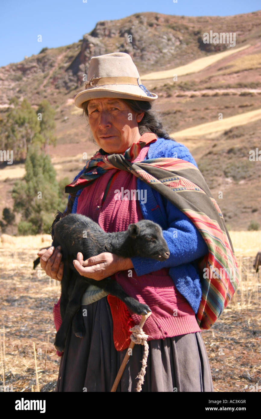 Quechuan shepherdess wearing traditional hat and brightly-coloured shawl holding 7-day-old lamb in Andes near Urubamba, Peru Stock Photo