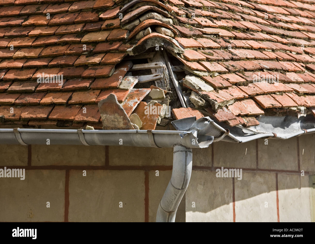 Damaged French red tile hipped roof with broken lead guttering  missing bonnet hip tiles and exposed roof timbers in saint valery sur somme france eu Stock Photo