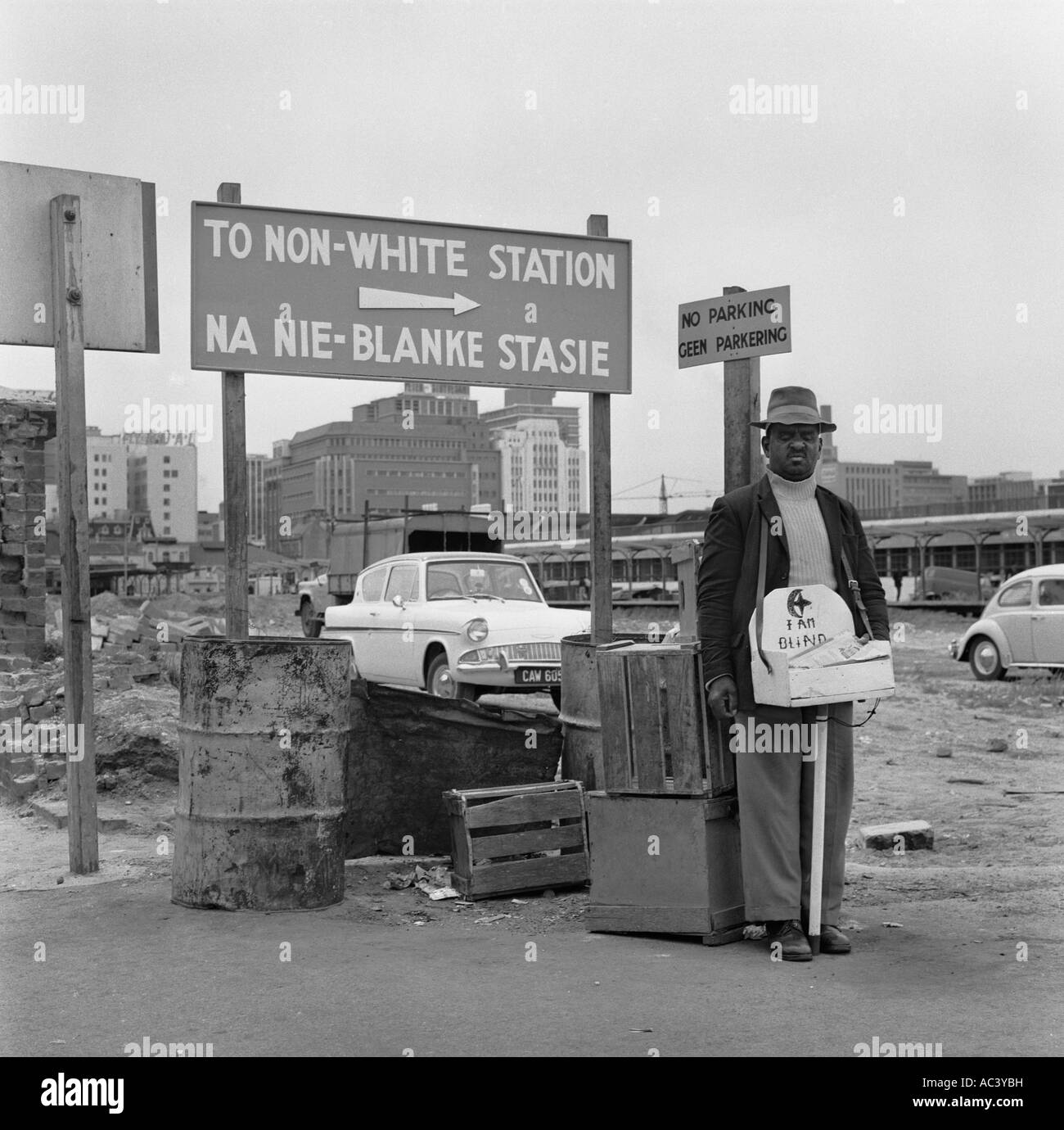Apartheid 1967 in Cape Town with blind beggar man standing by sign in waste ground indicating way to To Non White Station Stock Photo