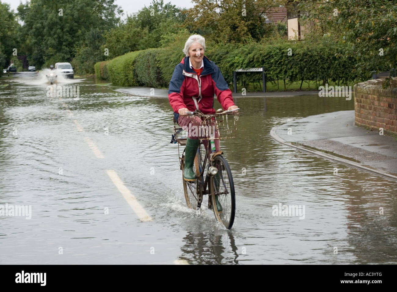 Smiling elderly woman riding bicycle riding through floods Tredington Tewkesbury UK Stock Photo
