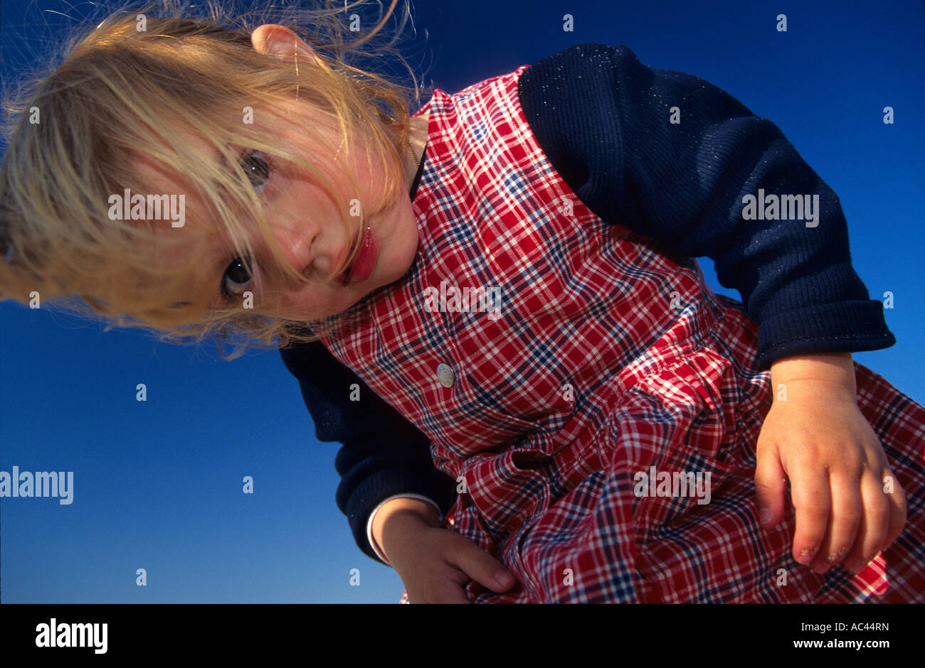A low-angle shot of a young girl intrigued by the camera. Portrait d'une fillette intriguée par l'appareil photographique. Stock Photo