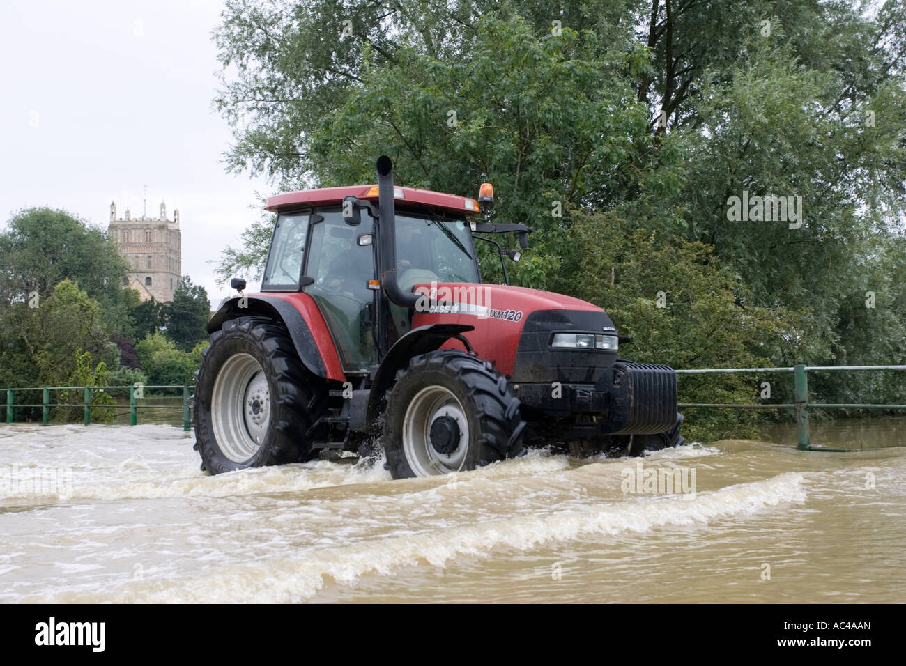 Red tractor driving along flooded road opposite Tewkesbury Abbey Gloucestershire UK Stock Photo