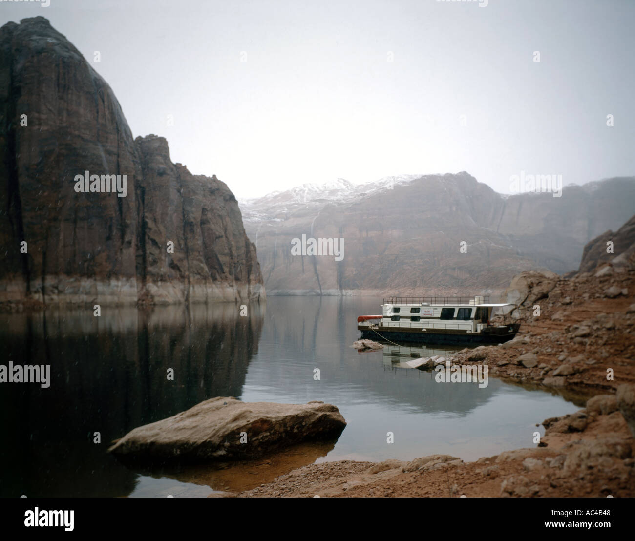 Lake Powell Reservoir on the Utah Arizona border showing a houseboat anchored in Iceberg Canyon during a Spring snowstorm Stock Photo