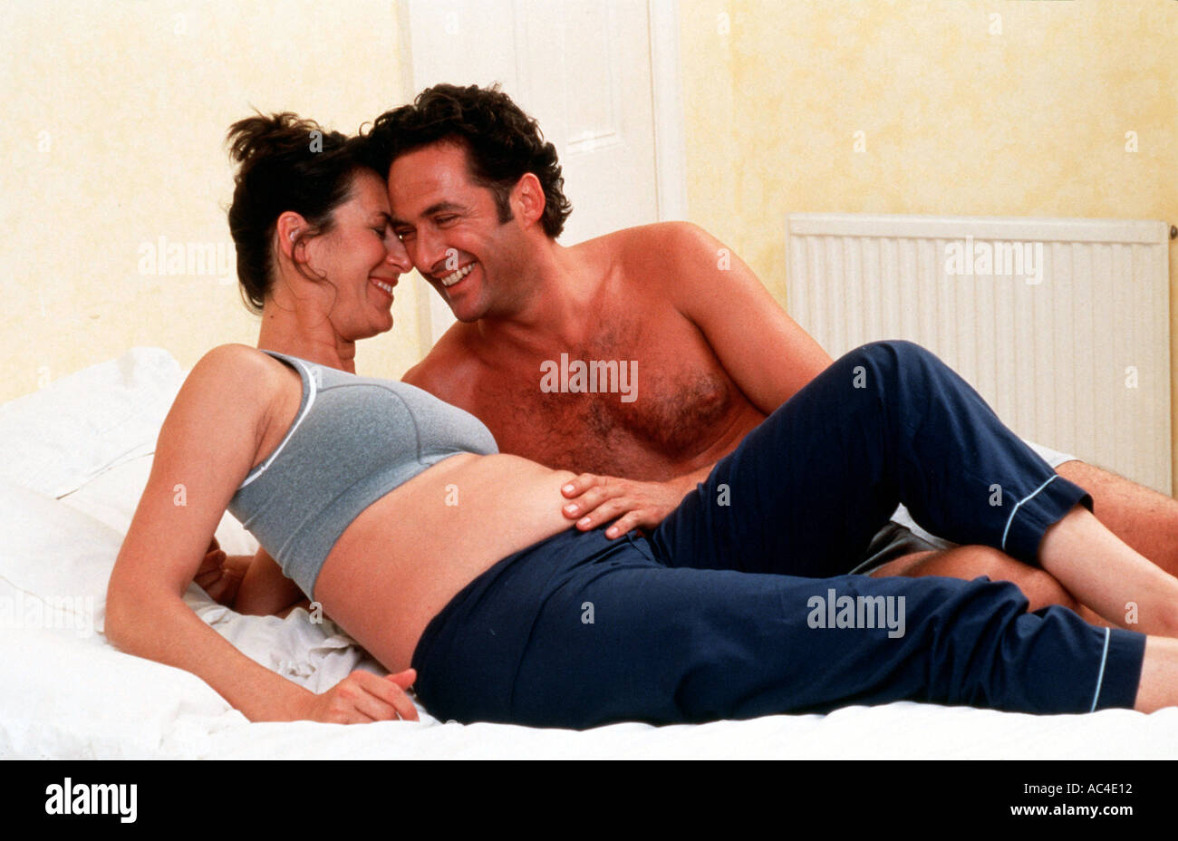W 18126 08 Model Released Pregnant couple lying on bed laughing Henry Arden RBO Stock Photo