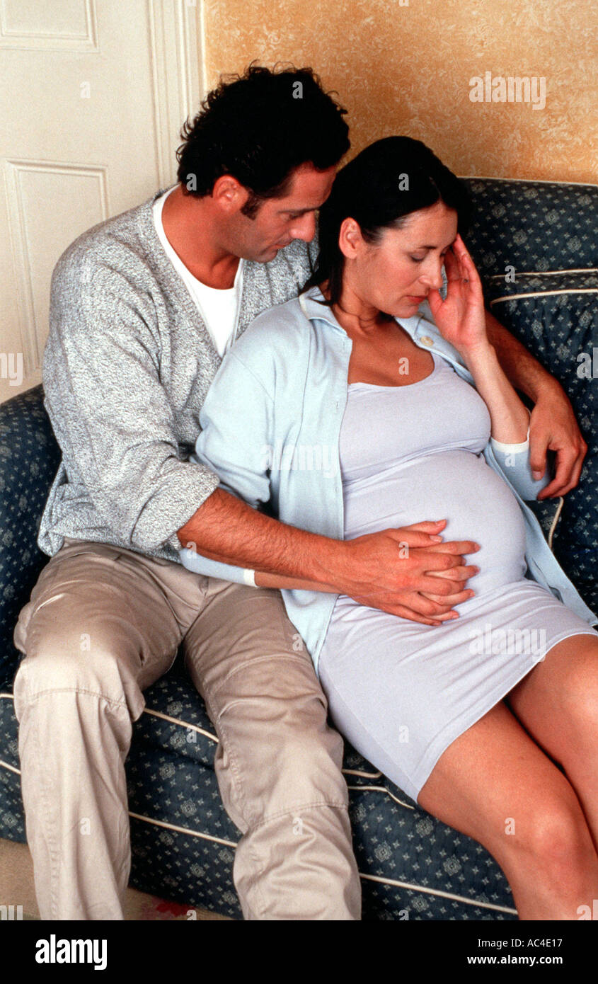 W 18126 32 Model Released Pregnant couple sitting on sofa hand to head Henry Arden RBO Stock Photo