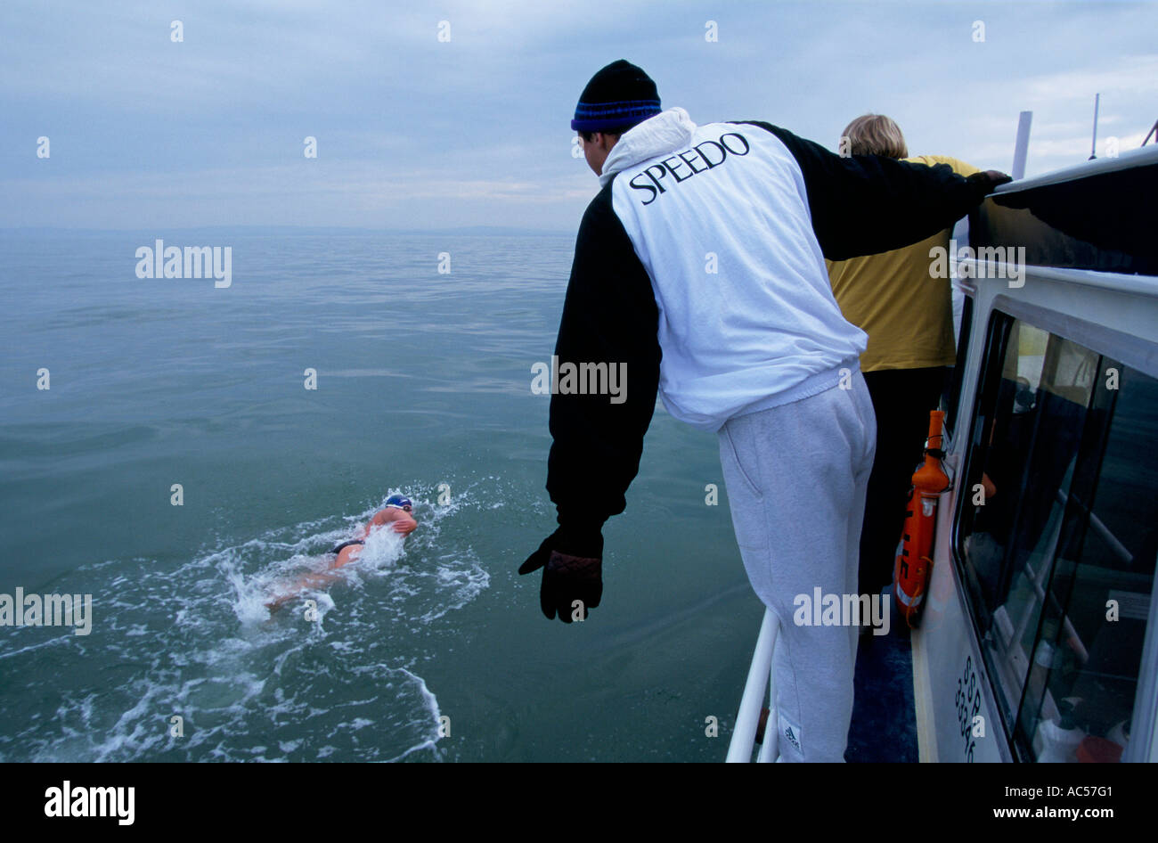 A MAN IN SPEEDO TRACKSUIT STANDS ON A BOAT EDGE WATCHING A MEMBER OF THE  BRITISH CROSS CHANNEL RELAY SWIMMING TEAM IN THE WATER Stock Photo - Alamy
