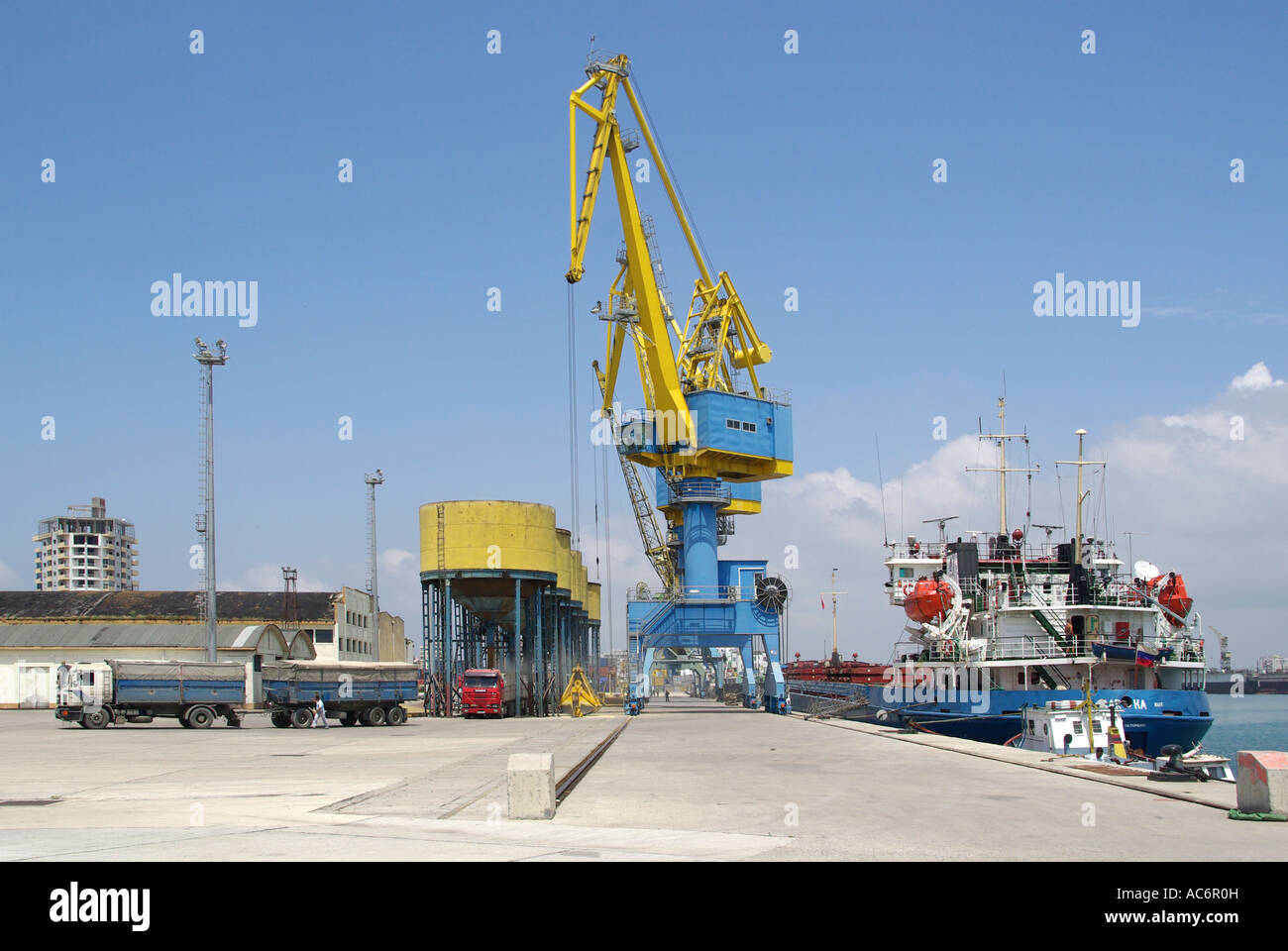 Durres Albania port on Adriatic coast yellow & blue cranes unload bulk carrier ship into grain silos on jetty & then into lorry truck transport below Stock Photo