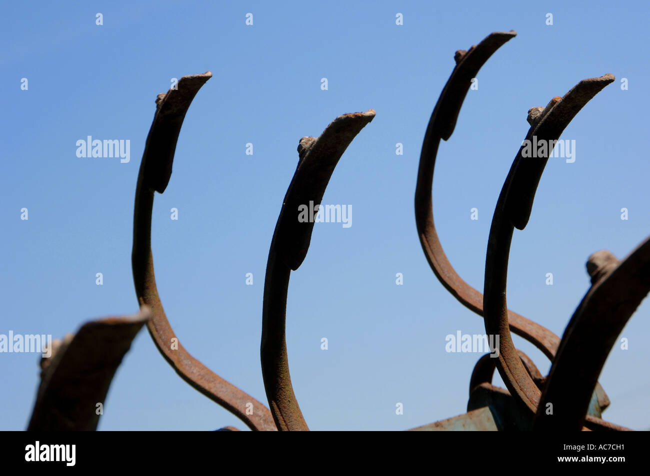 Old farm machinery makes a pattern like clawed fingers against a blue summer sky Stock Photo