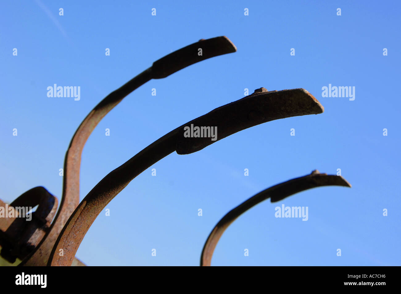 Old farm machinery makes a pattern like clawed fingers against a blue summer sky Stock Photo