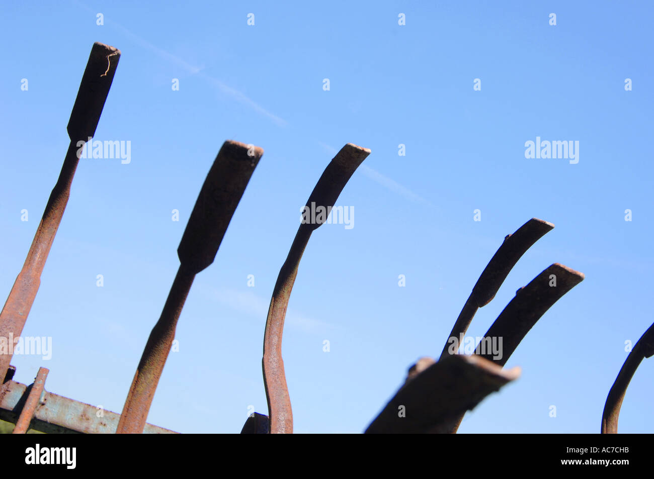 Old farm machinery makes a pattern like clawed fingers against a blue summer sky Stock Photo