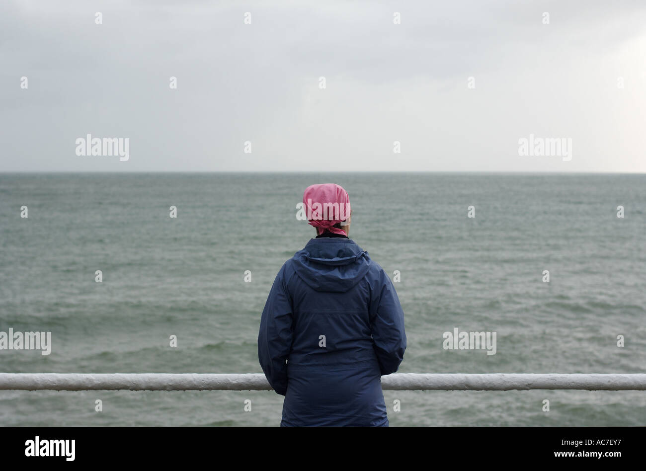 woman in a pink hat looking out over Cardigan Bay Aberystwyth, standing alone, lonely, by herself Stock Photo