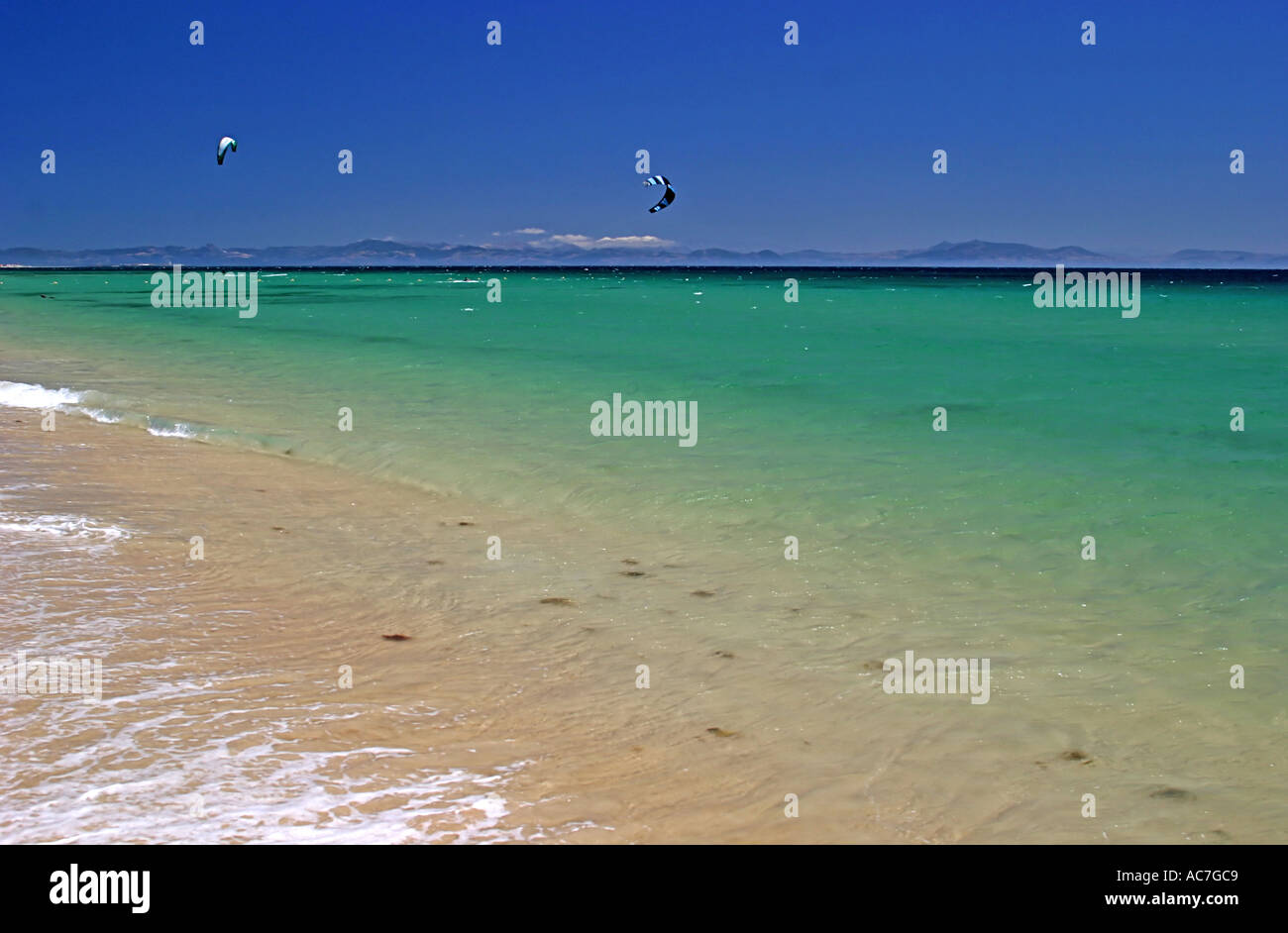 Waves gently lapping on a white sandy Spanish beach in the hot summer with dark blue skies Stock