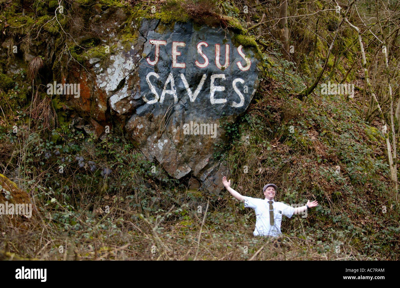Mormon missionary posing under JESUS SAVES graffiti on exposed rock