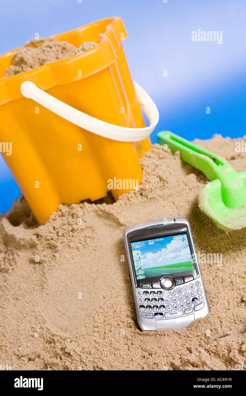 a blackberry mobile phone on the beach with sand and a bucket and spade working on holiday Stock Photo