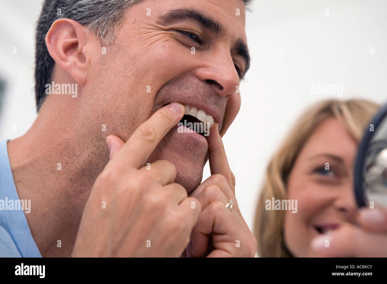Close-up of a mature man applying a teeth whitening strip to his teeth with a mid adult woman beside him Stock Photo