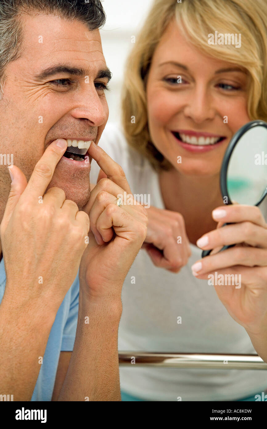 Close-up of a mature man applying a teeth whitening strip to his teeth with a mid adult woman holding a mirror Stock Photo